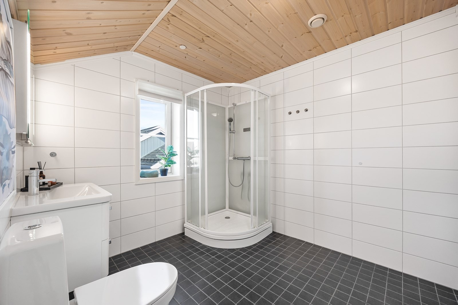 Badet er innredet med toalett, dusjkabinett, servant i baderomsinnrending og speil med integrert belysning. Galleribilde