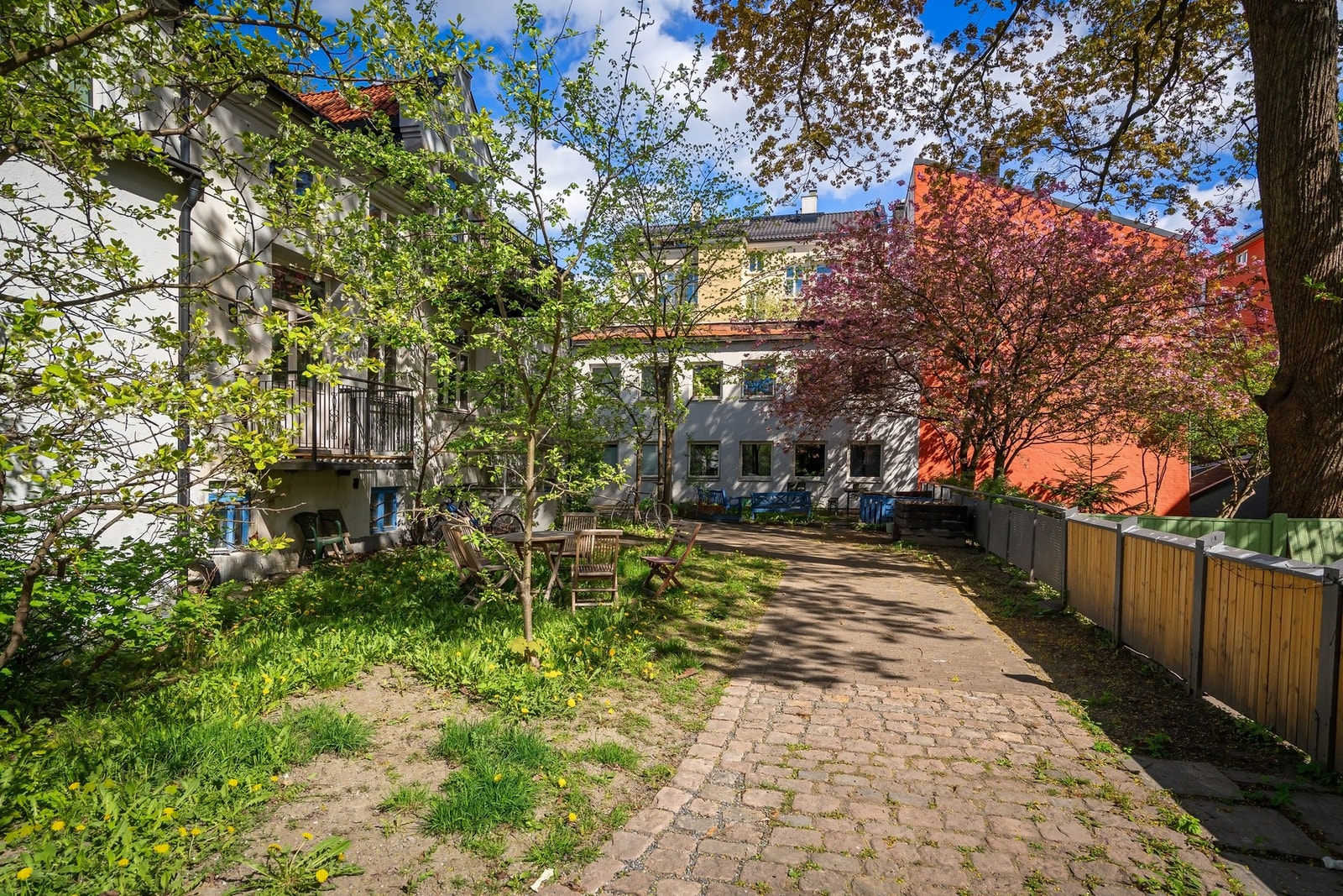 Koselig bakhage med sittegrupper, brostein og gressplen samt diverse beplantning. Galleribilde