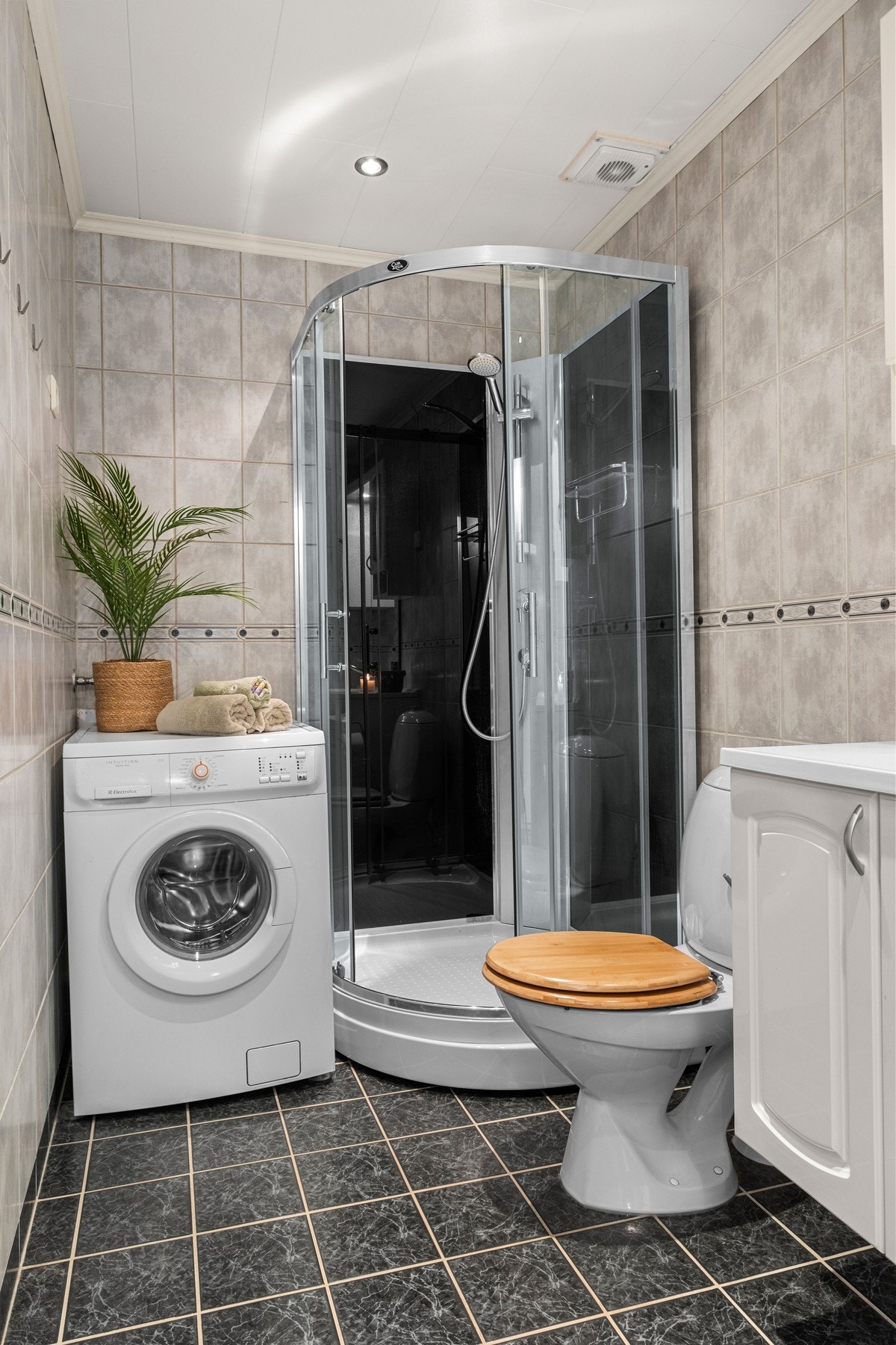 Badet er innredet med servantinnredning, gulvmontert toalett, opplegg for vaskemaskin og dusjkabinett. Galleribilde