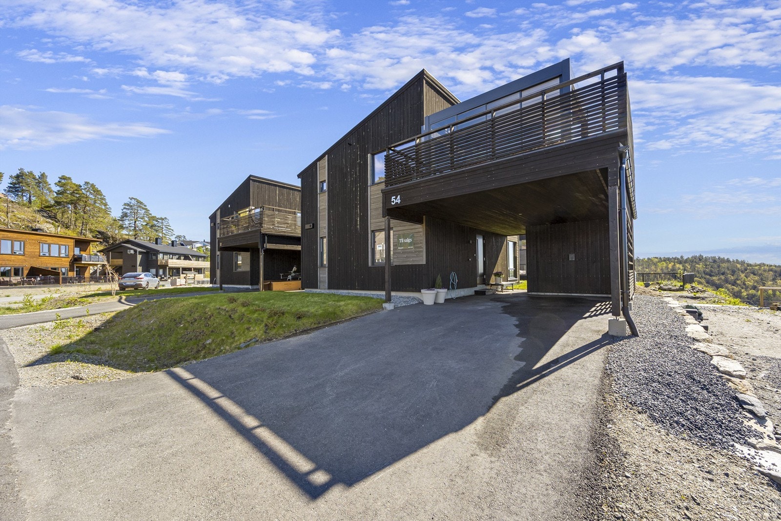 Det er asfaltert innkjørsel og carport med bod i enden. Elbillader er installert på vegg til boden. Galleribilde