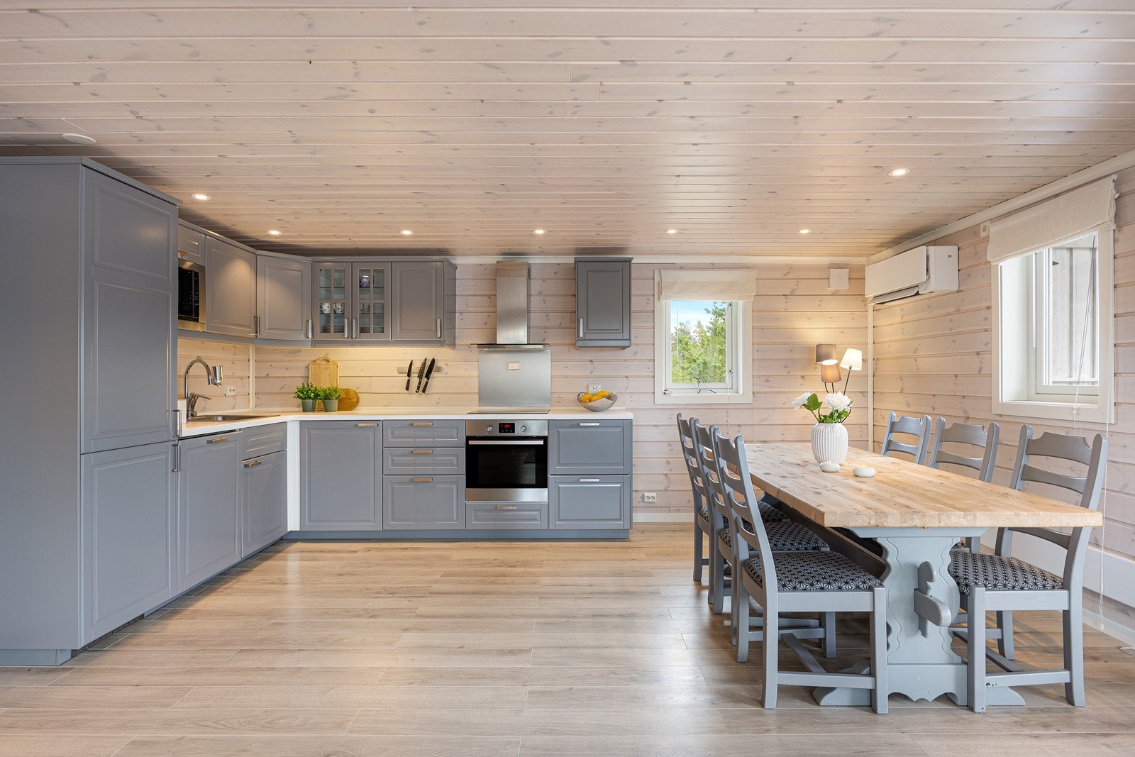 Innredningen har grå, profilerte fronter, vitrineskap, nedfelt oppvaskkum og laminert benkeplate i hvitt design. Galleribilde