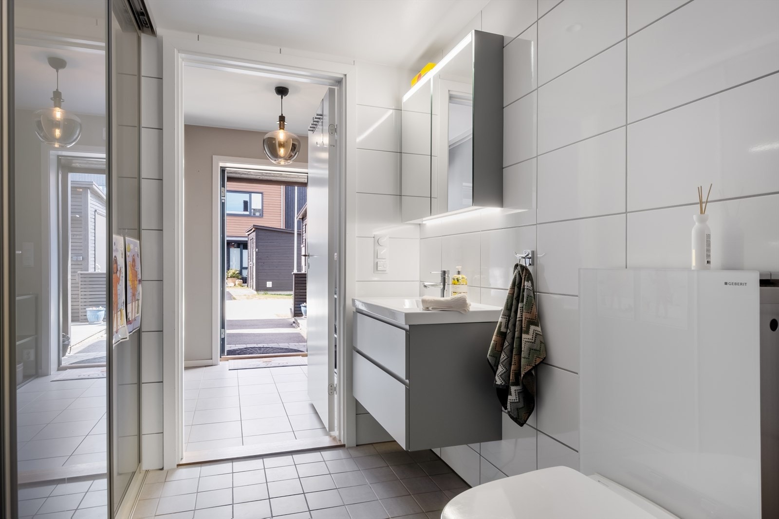 Badet er funksjonelt innredet med dusjhjørne med innfellbare glassdører, veggmontert toalett og servantskap med hvit servant og tilhørende blandebatteri. Galleribilde