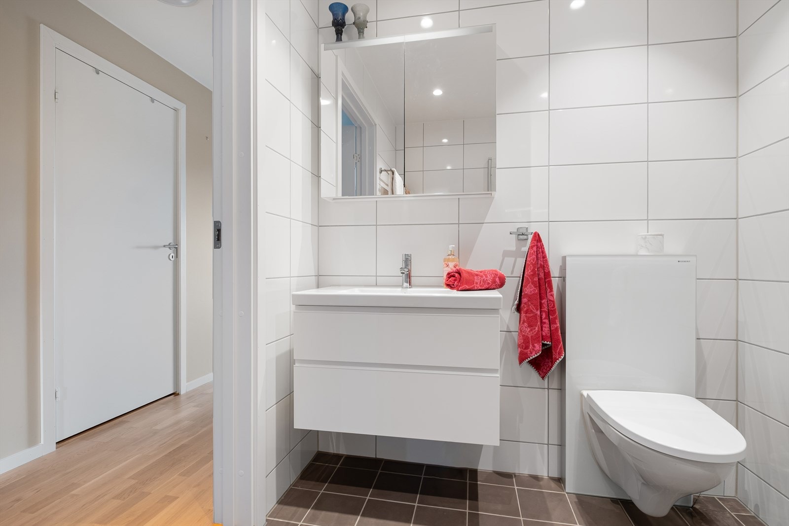 Badet er funksjonelt innredet med dusjhjørne med innfellbare glassdører, veggmontert toalett og servantskap med integrert servant og armatur Galleribilde