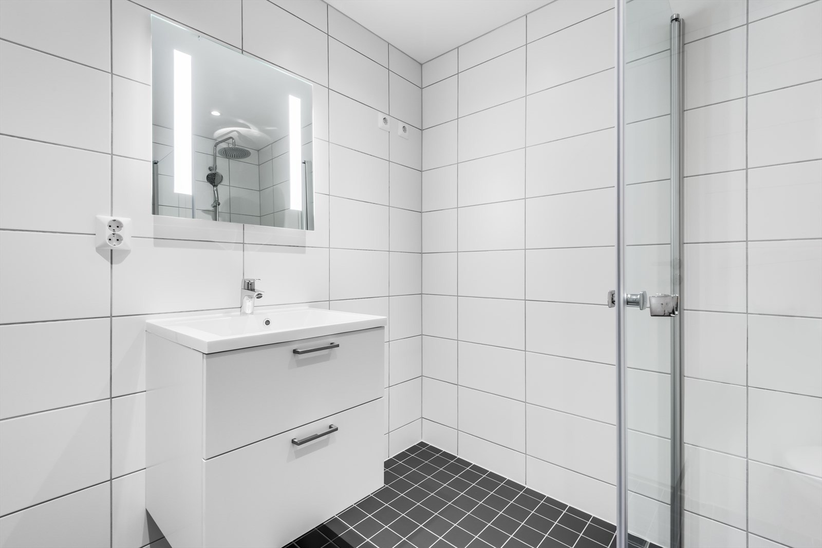 Rommet fremstår delikat og tidløst med lyse fliser på vegger og gulv, varmekabler og downlights. Fotograf: EFKT Galleribilde