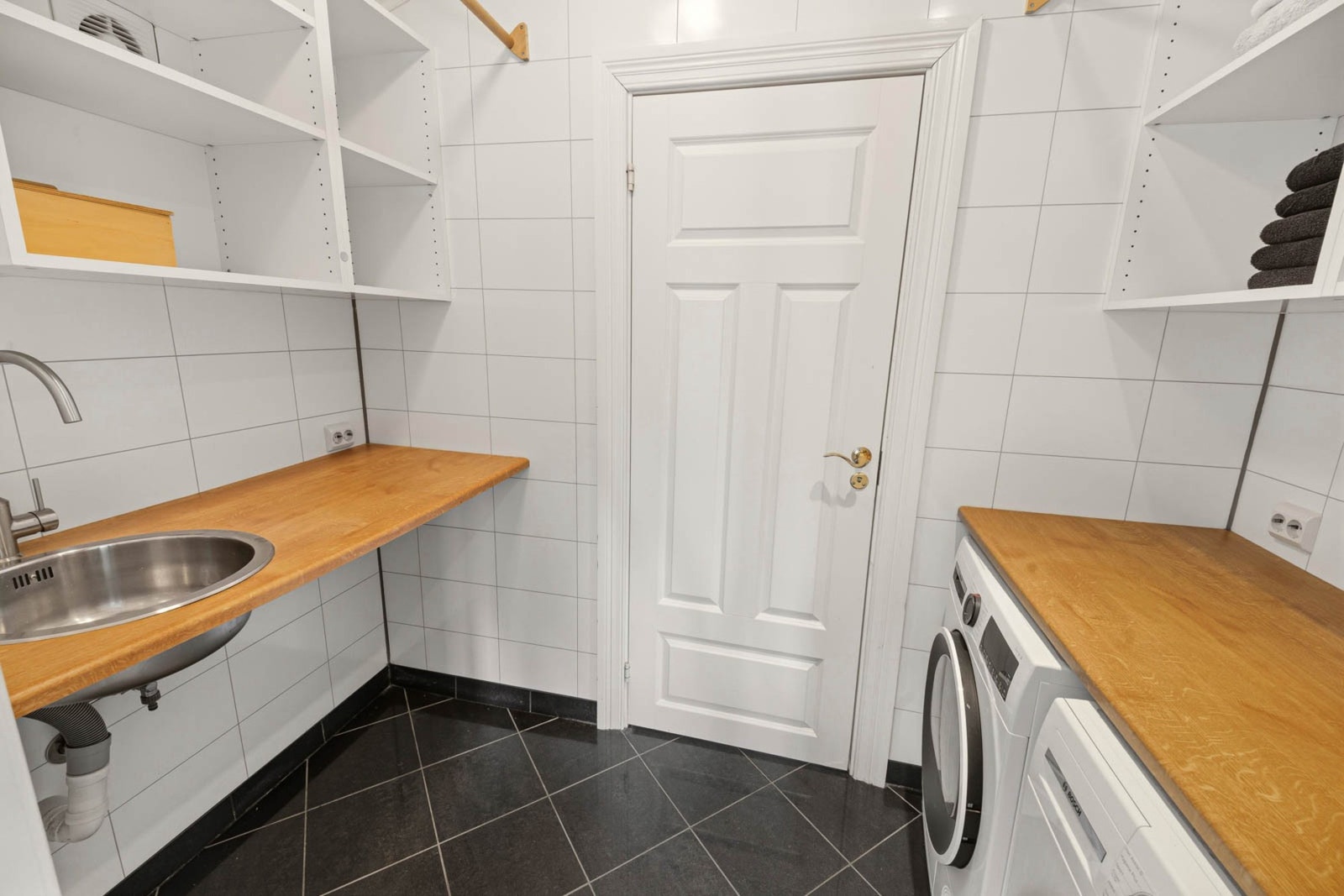Rommet har god benkeplass med utslagsvask, gode oppbevaringsmuligheter og plass til både vaskemaskin og tørketrommel. Galleribilde
