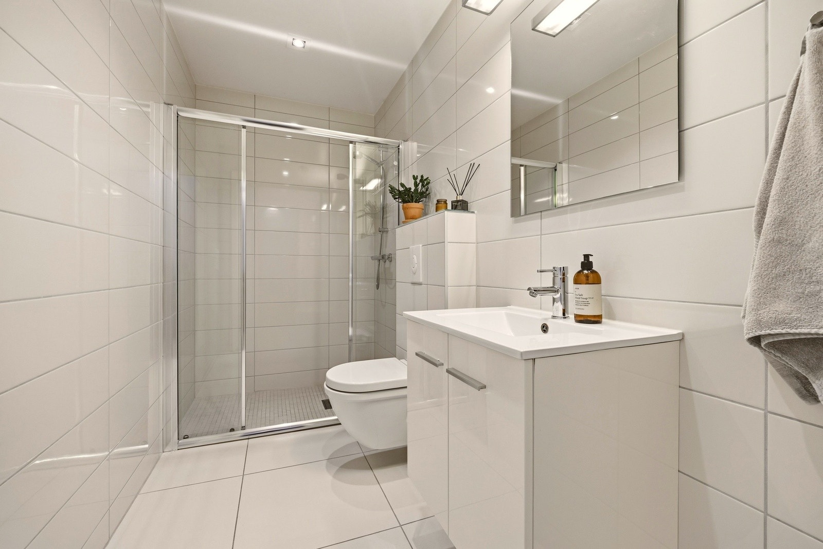 Badet er funksjonelt innredet med servantseksjon, dusjnisje med skyvedører i herdet glass, vegghengt toalett og speil. Galleribilde