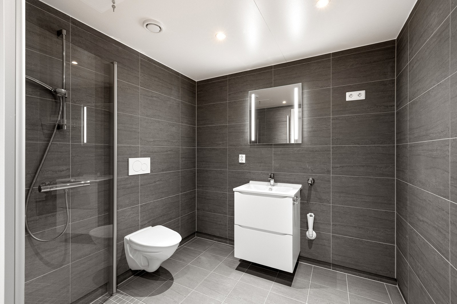 Badet holder en gjennomført og moderne standard med flislagte overflater i elegante gråtoner som skaper et stilrent uttrykk. Galleribilde