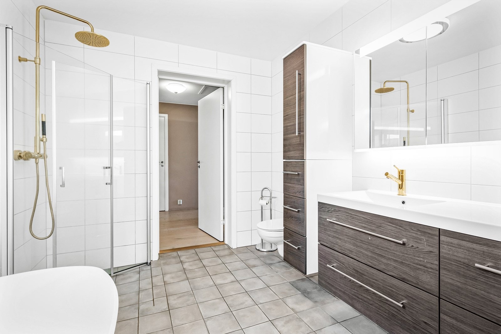 Badet er utstyrt med dobbel servant med underskap, veggskap, speil med lys, toalett, dusjnisje med regndusj og frittstående badekar Galleribilde