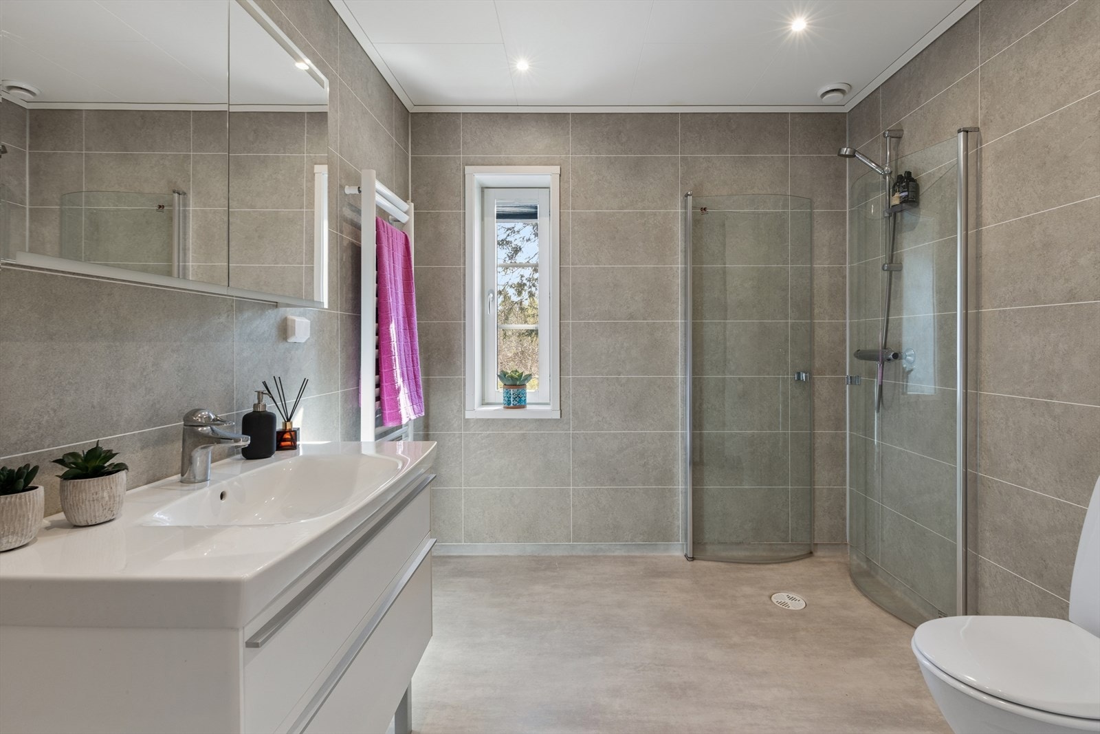 Badet i første etasje har baderomsplater på veggene, vinyl på gulv, dusjhjørne med glassdører og håndkletørker. Galleribilde