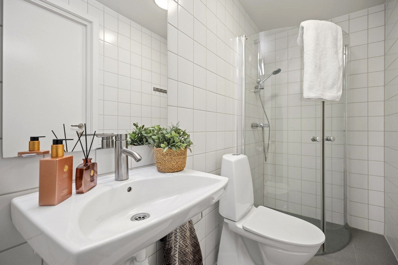 Praktisk og helfliset bad med et tidløst uttrykk. Badet er utstyrt med dusjløsning med glassdører, toalett og servant med oppbevaringsmuligheter. Varmekabler i gulvet gir god komfort i hverdagen. Galleribilde