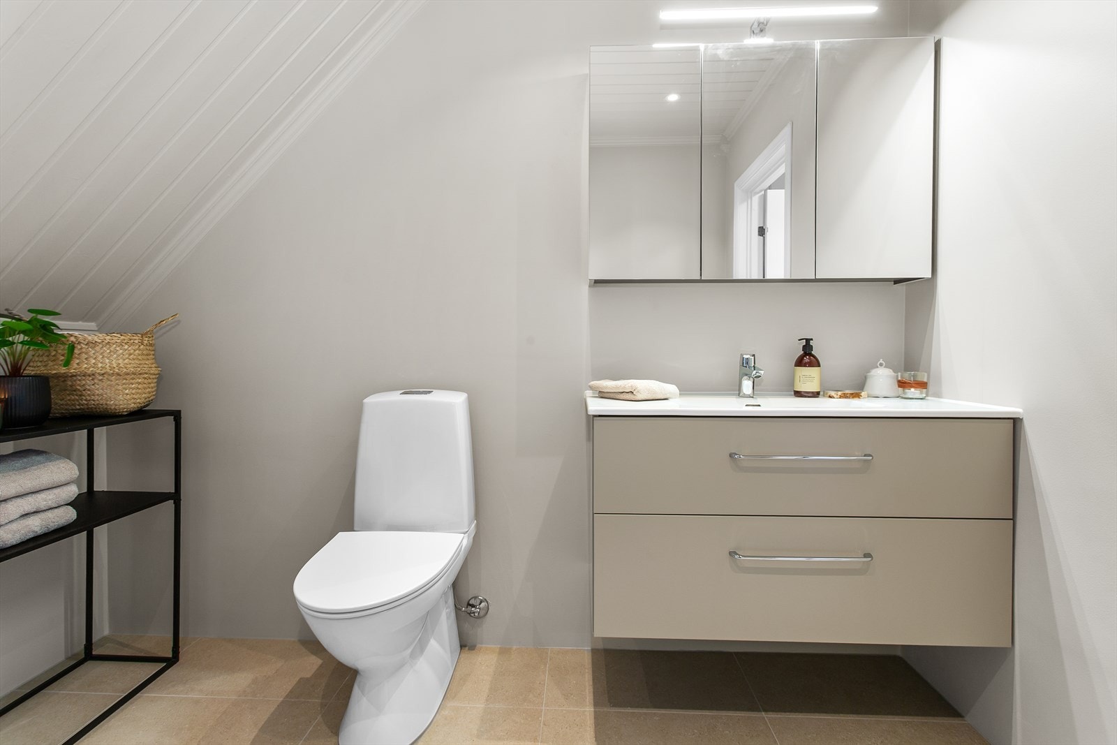 Badet har flislagt gulv med undervarme, innredning med heldekkende servant, skuffer, speilskap og belysning samt wc, dushjørne og opplegg for vaskemaskin Galleribilde