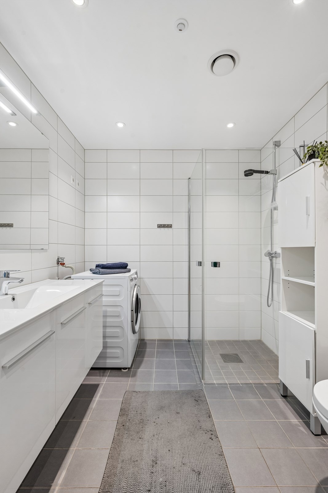 Badet har dusjhjørne med glassvegger, vegghengt toalett og opplegg for vaskemaskin. Galleribilde