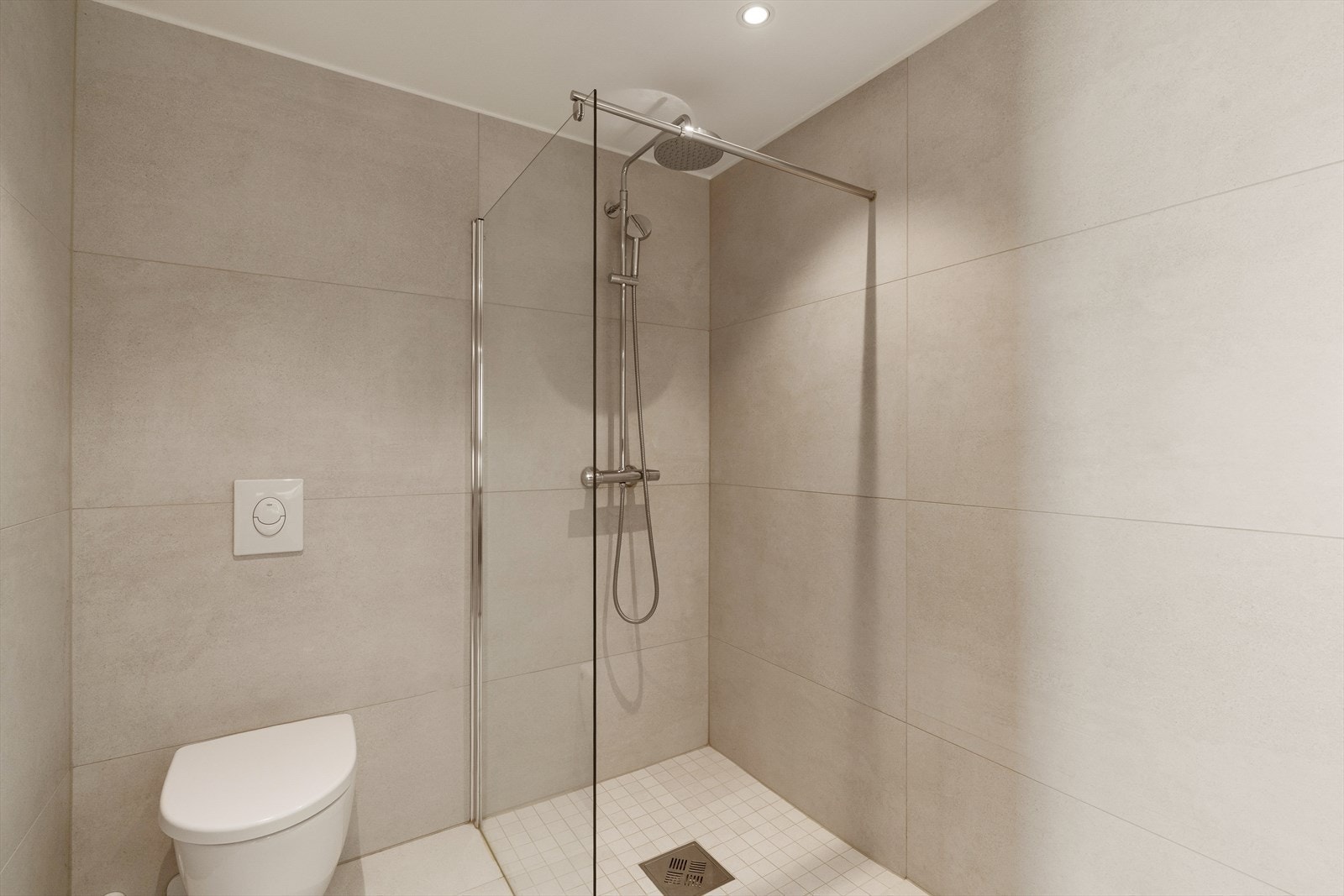 Badet inneholder dusjhjørne med glassvegger, vegghengt toalett, servant i baderomsinnredning, samt opplegg for vaskemaskin og tørketrommel. Galleribilde