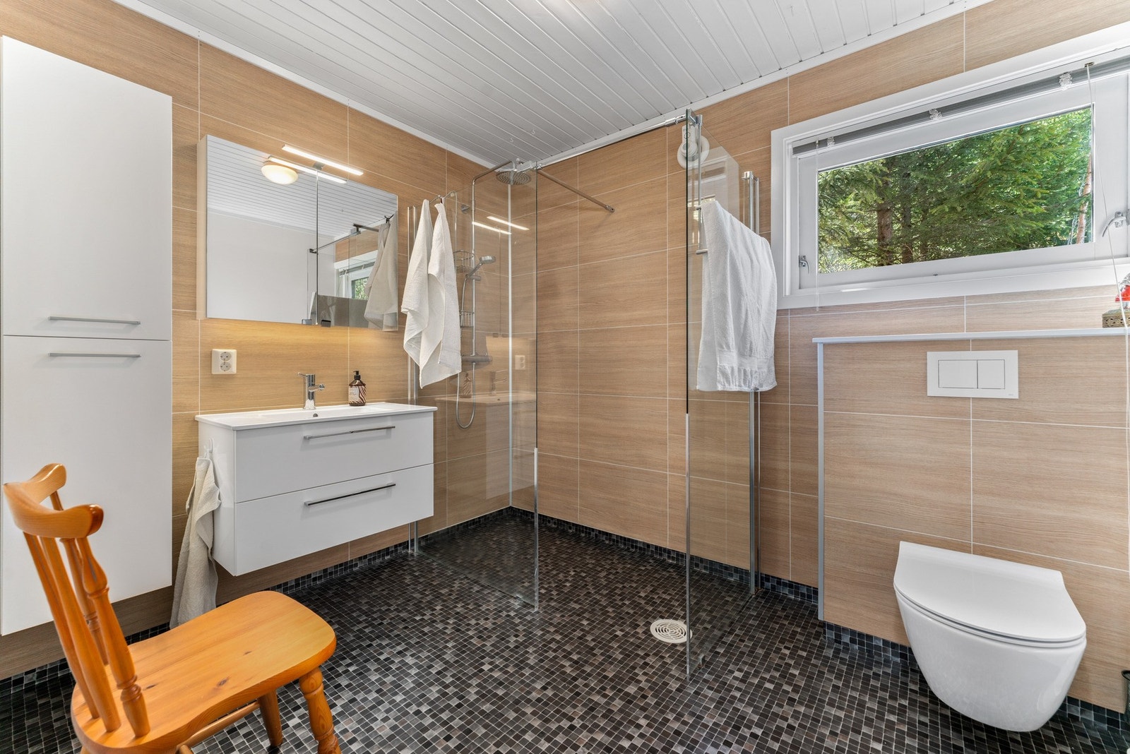 Badet i 1. etasje ble oppgradert i 2019 og fremstår lyst og romslig. Her er det baderomsplater på vegger, panel i himling og vinylbelegg på gulv med vannbåren gulvvarme. Galleribilde