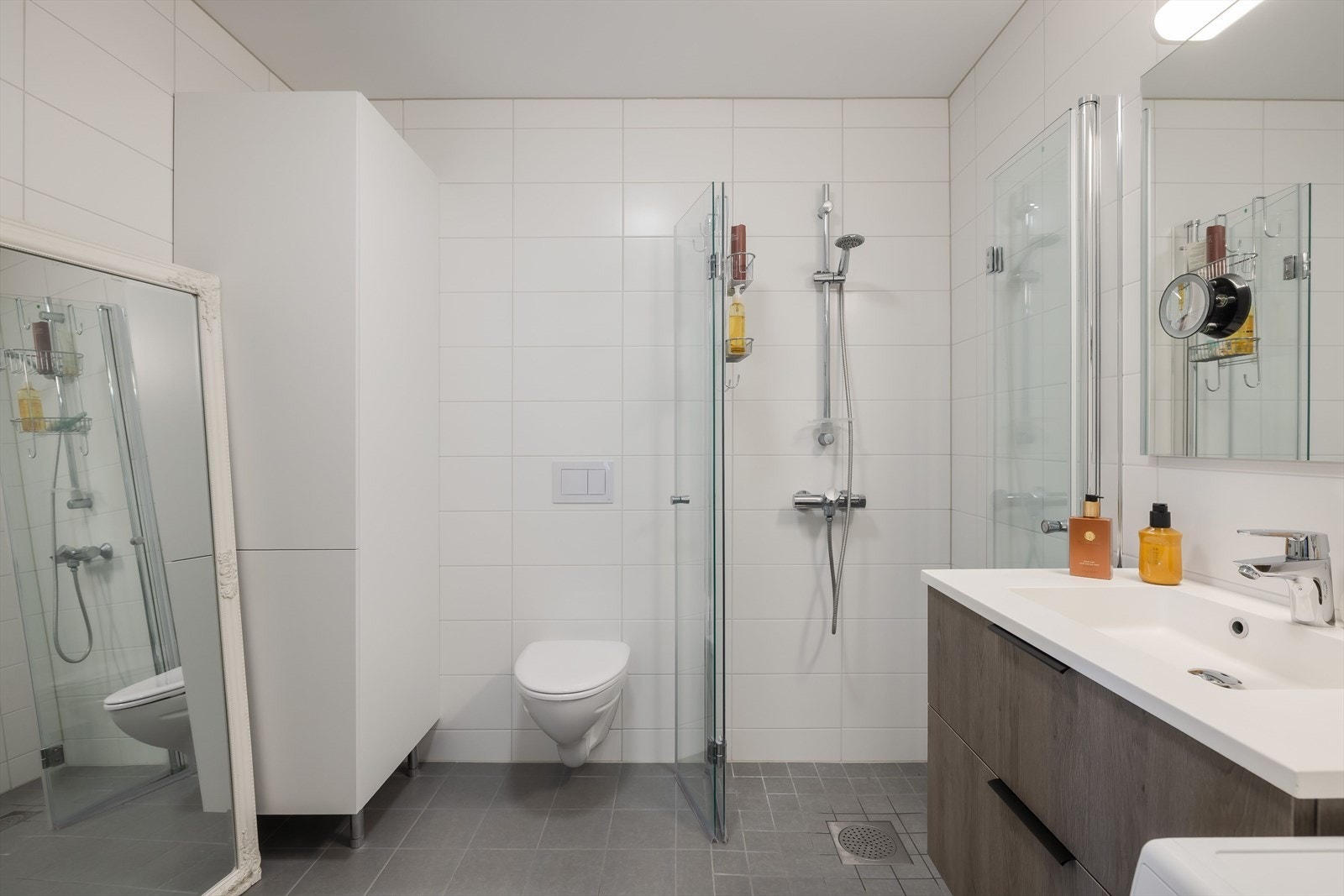 Badet har veggmontert toalett, dusjhjørne med innfellbare dusjdører og baderomsinnredning med skuffer og heldekkende servant. Galleribilde