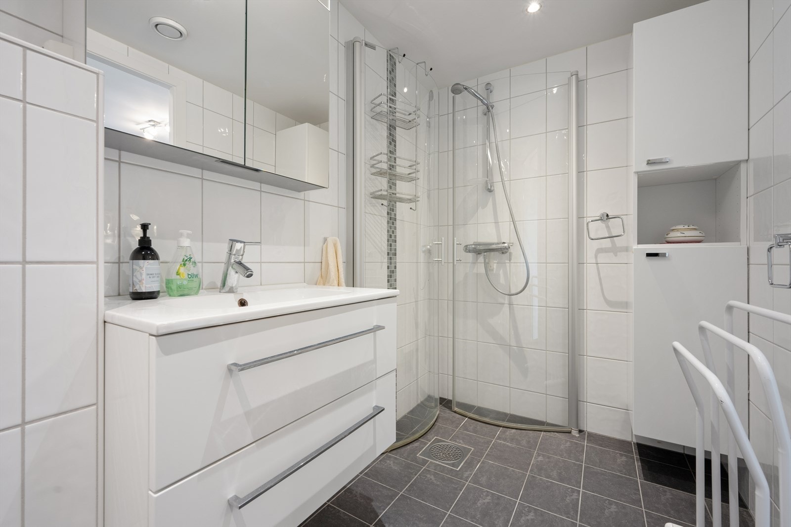 Badet er fra 2010 og er tidløst innredet med grå fliser på gulvet og hvite fliser på vegg. I gulvet har man også varmekabler for ekstra komfort. Badet er ellers utstyrt med dusjhjørne, vegghengt toalett og baderomsinnredning med nedfelt servant. Galleribilde