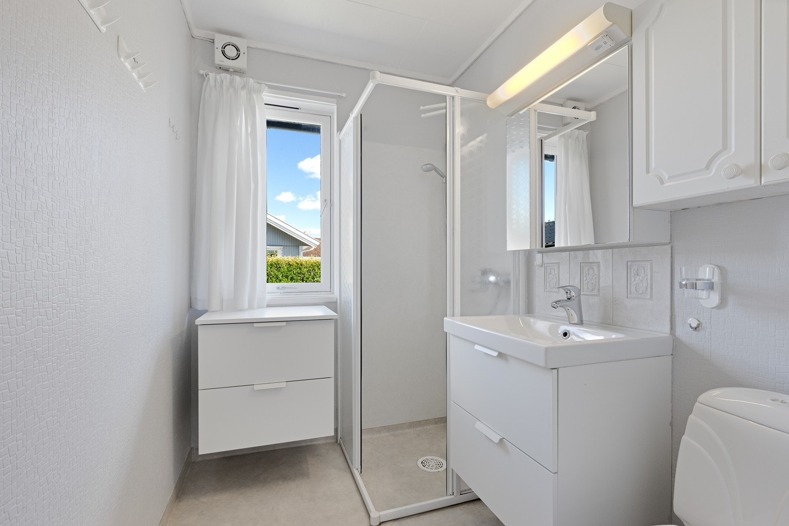 Badet har vinylbelegg på gulvet og våtromstapet på veggene, samt en elektrisk vifte som sørger for ventilasjon. Galleribilde