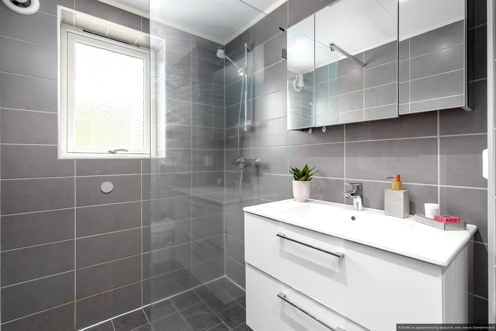 Badet er utstyrt med innredning med nedfelt servant, vegghengt skap med speil, toalett og dusjhjørne Galleribilde