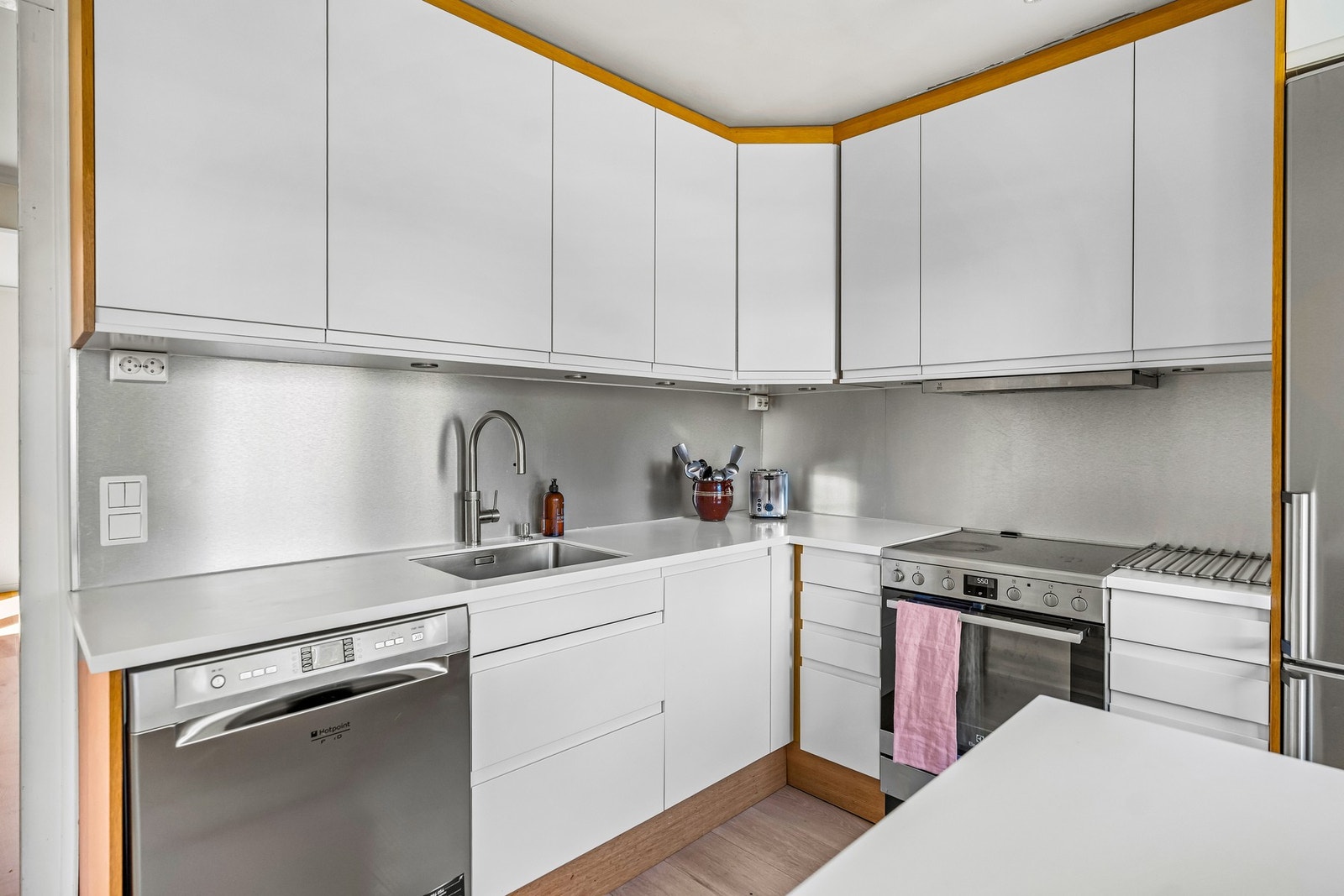 Kjøkkenet har en benkeplate i Corian Glacier White med underlimt Blanco-vask, samt ettgreps kjøkkenarmatur av typen Quooker Flex i rustfritt stål med uttrekk og Pro3-beholder. Mellom benkeplate og overskap er det montert dekorative metallplater på veggene Galleribilde