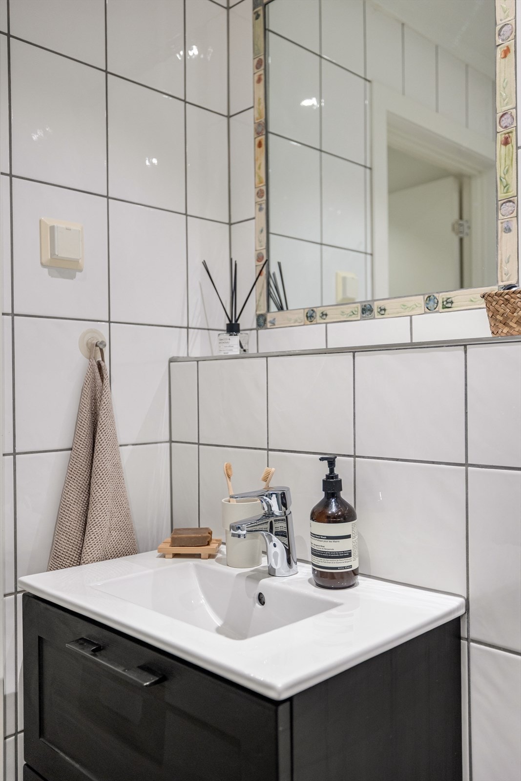 Badet er utstyrt med vegghengt servantinnredning med glatte fronter, heldekkende servant og ettgreps armatur. Det er speil innfelt i flis over servant. Dusjhjørne med innfellbare glassdører, dusjarmatur med hånddusj og vegghengt toalett. Galleribilde