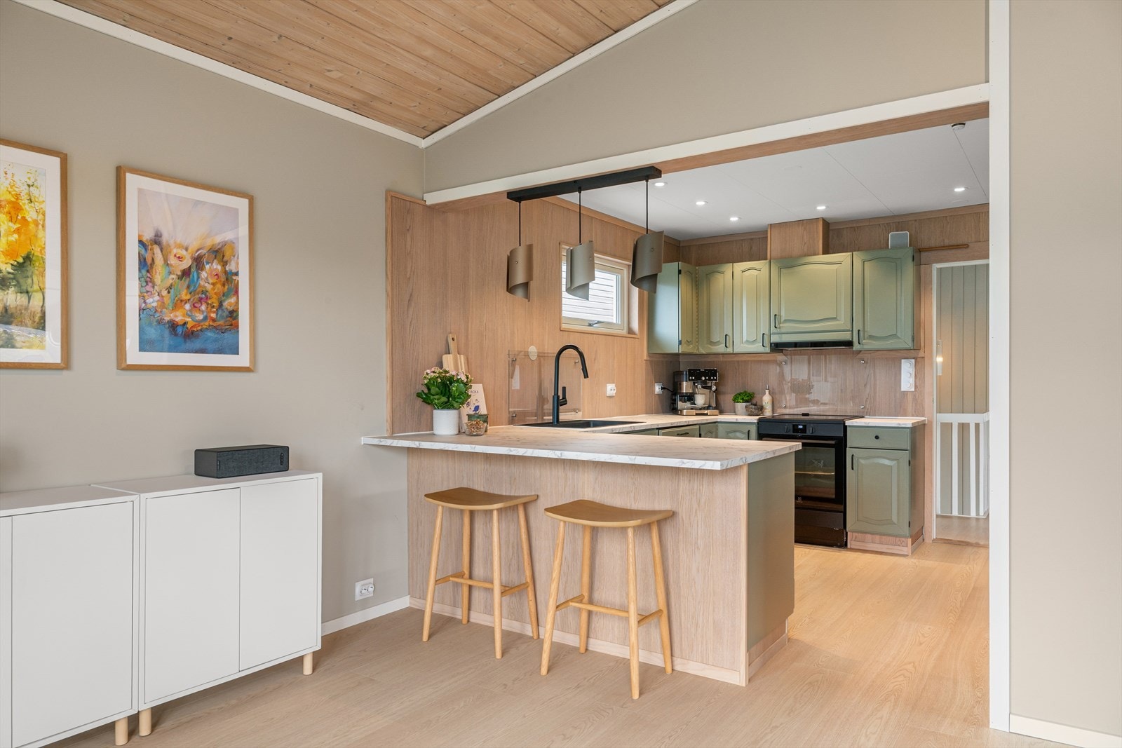 Kjøkkenet ligger i delvis åpen løsning med stuen og er innredet med profilerte, grønnmalte fronter og lys benkeplate i laminat. Galleribilde