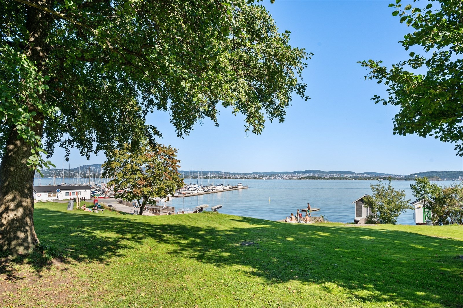 Oksvalstranda med gresslette, sandstrand, båthavn og brygge. Galleribilde