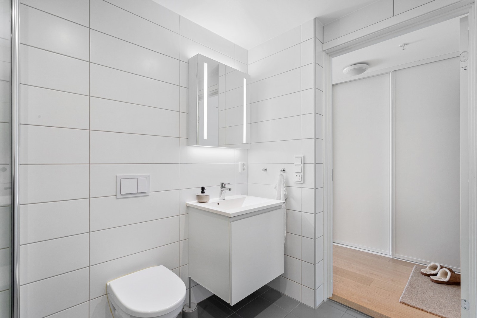 Badet er utstyrt med vegghengt WC, moderne speilskap og dusjhjørne med innfellbare dører. Galleribilde