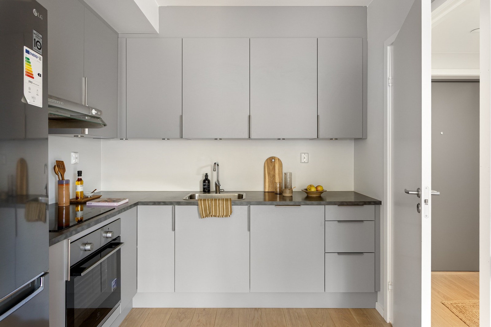 Grå, glatt innredning med laminat benkeplate og kum i rustfritt stål med ett-greps armatur. Galleribilde