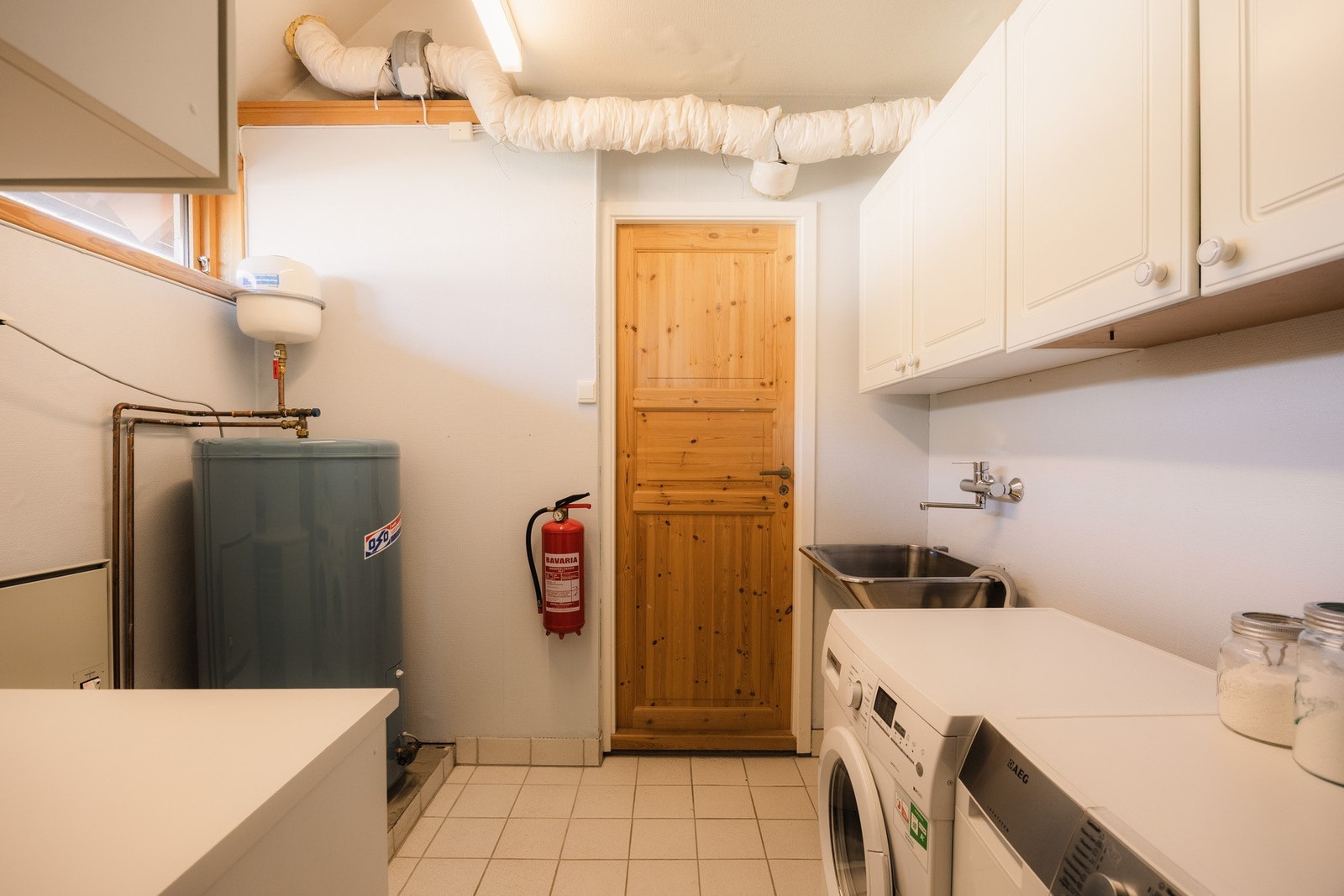 Funksjonelt vaskerom med flislagt gulv, tapetserte vegger og sluk. Opplegg for både vaskemaskin og tørketrommel, vegghengt utslagsvask og varmtvannspreder på 200L. Bak døren er det et praktisk tørkerom. Galleribilde