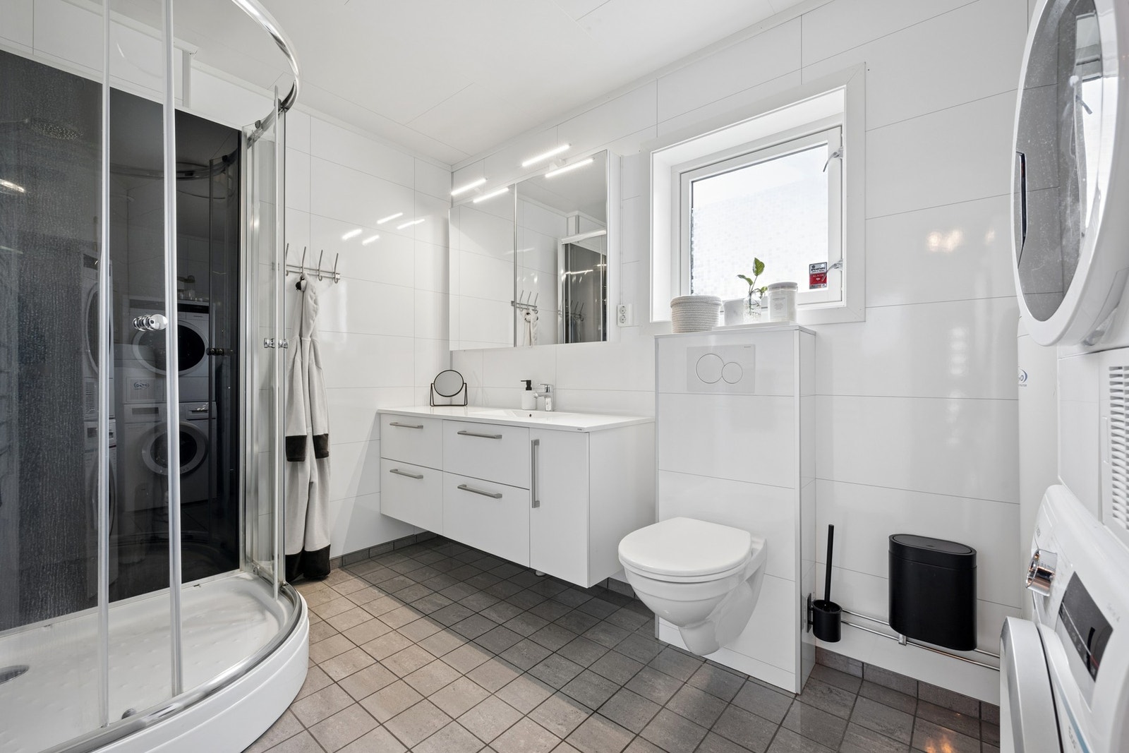Stilrent bad med gulvvarme, med en praktisk innredning, vegghengt toalett og opplegg for vaskemaskin. Galleribilde