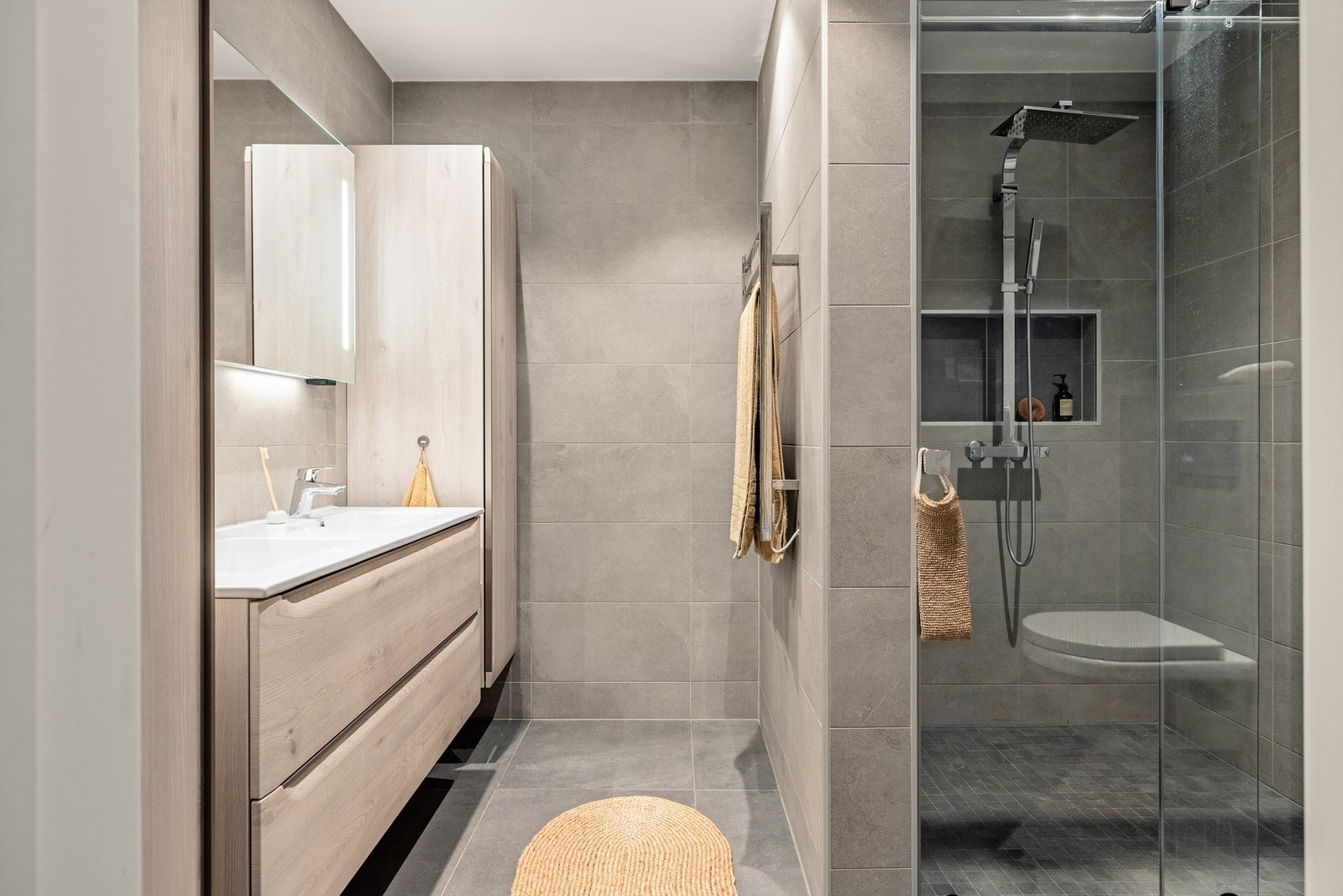 Badet er innredet med vegghengt toalett, dusjnisje med ganityr, nisje og glassdør, og baderomsmøblement med speil, belysning og høyskap. Galleribilde