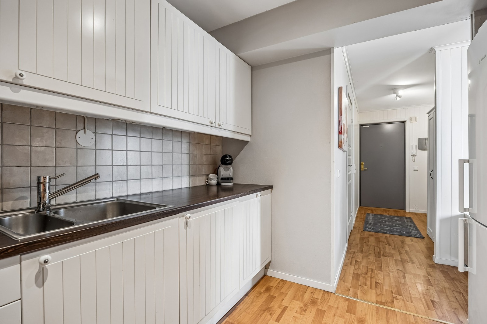 Tidløst kjøkken med hvite fronter, integrerte hvitevarer som oppvaskmaskin, komfyr og koketopp. Galleribilde