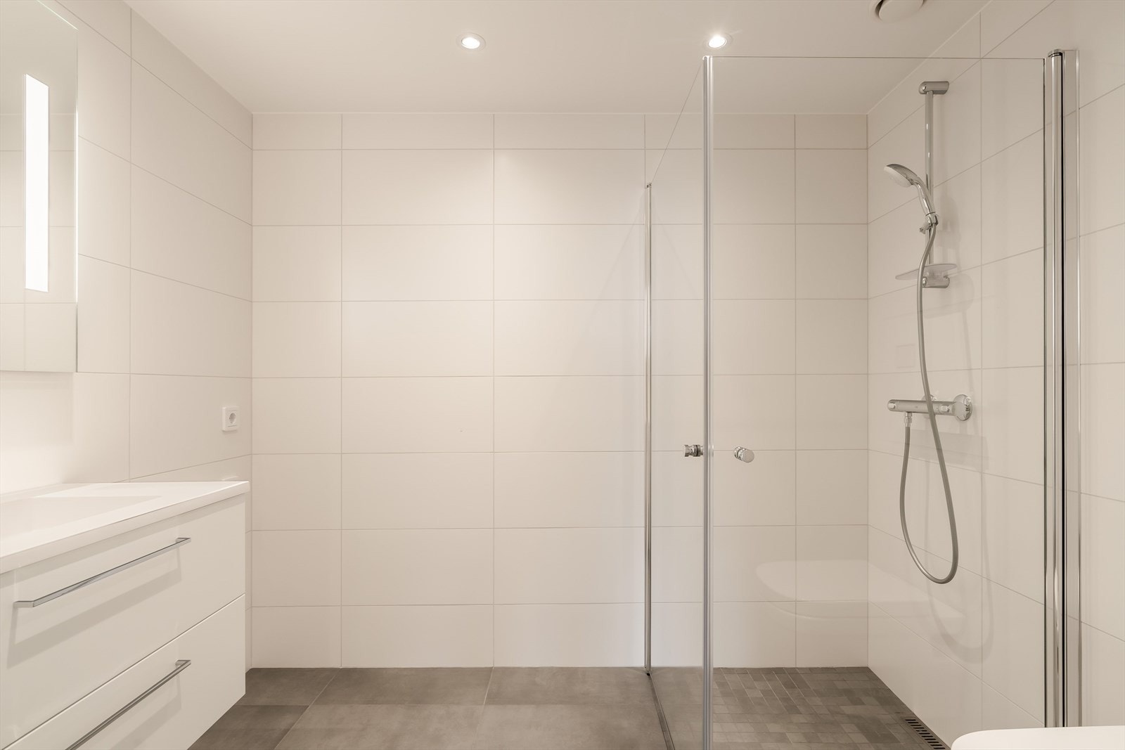 Innredningen består av servant med skuffer og speil med belysning. Videre er badet utstyrt med dusjhjørne, vegghengt toalett og downlights i himling for et stilrent uttrykk. Galleribilde