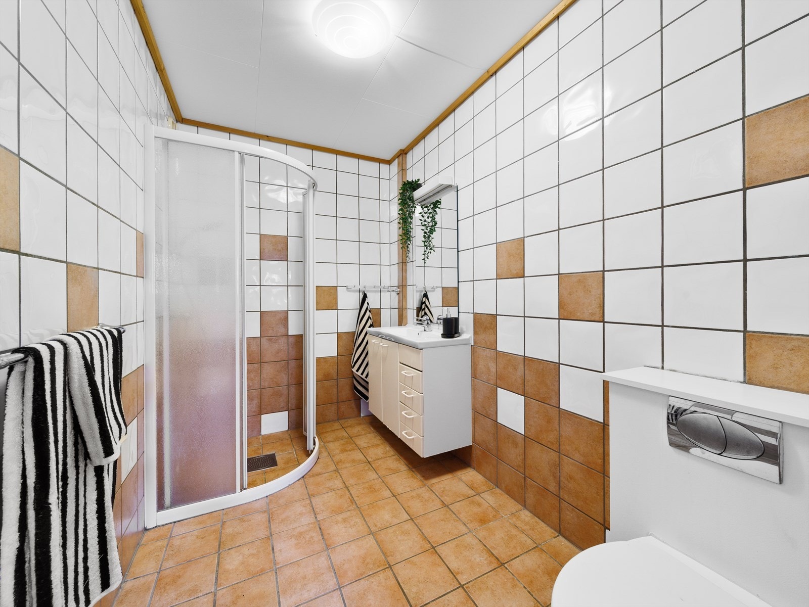 Helflist bad som er innredet med dusjvegger, toalett og hvite baderomsmøbler med speil. Galleribilde
