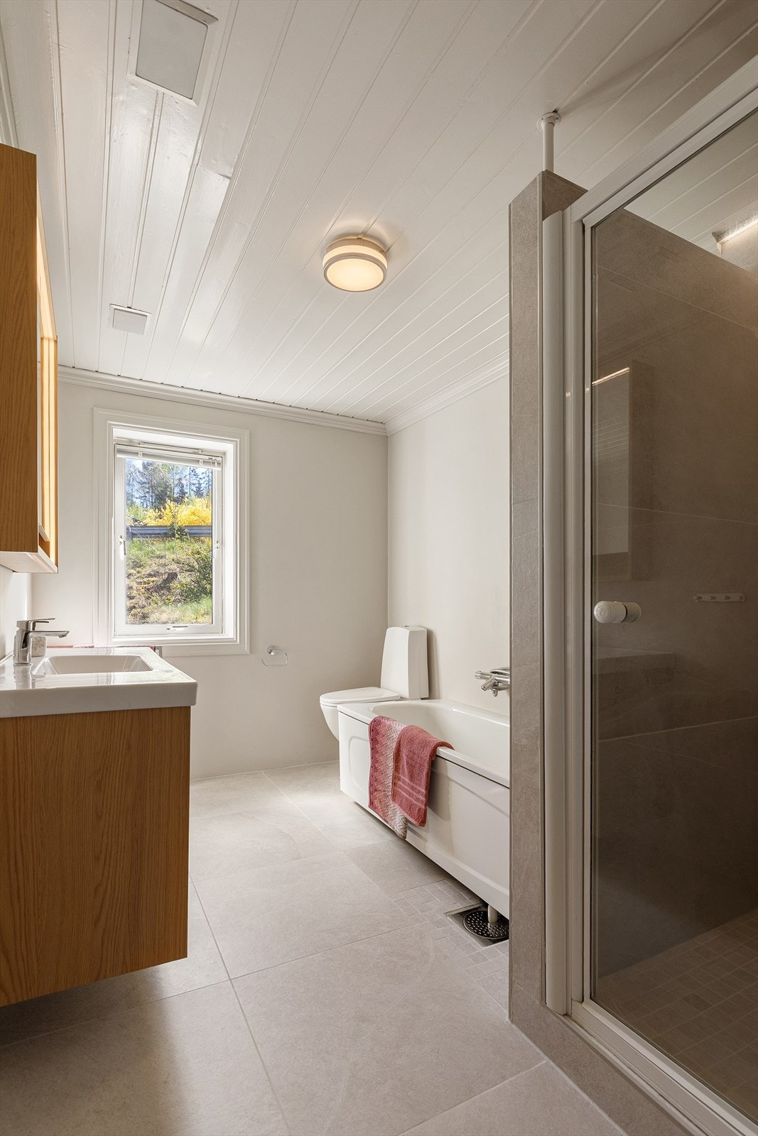 Badet er innredet med vegghengt servantskap, speilskap, gulvstående toalett, badekar, og flislagt dusjnisje Galleribilde