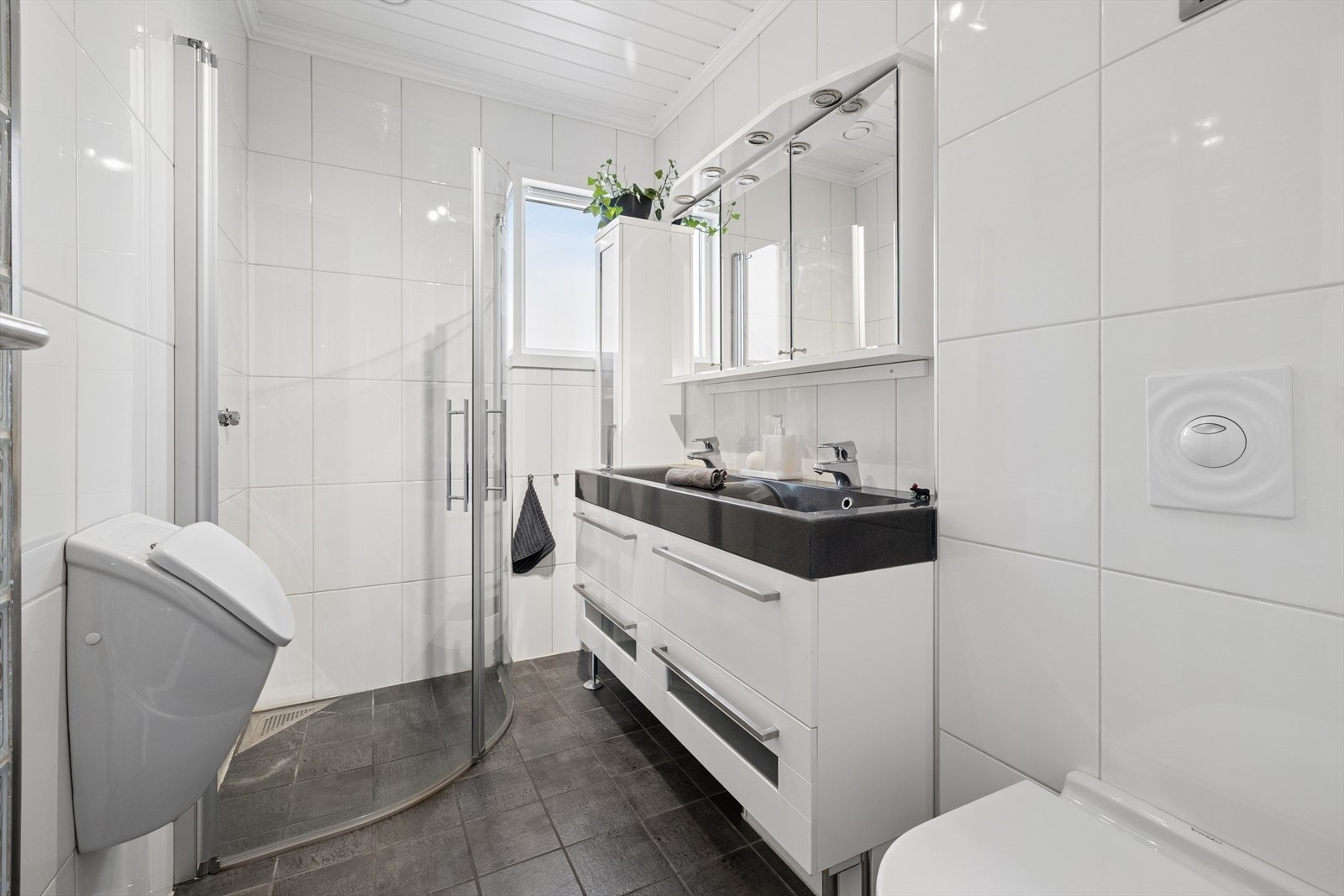 Badet i første etasje har flislagt gulv med varmekabler, vegghengt toalett, urinal og dobbel servant. Galleribilde