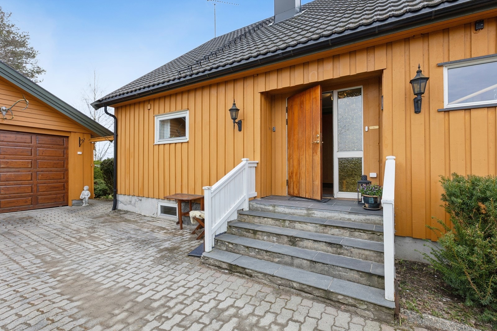 Et solid inngangsparti med trapp av betong belagt med skifer. Hovedytterdøren er i teak. Galleribilde