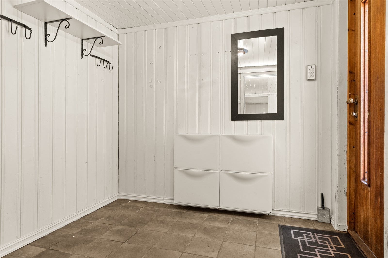 Vel inne er en lys gang med flislagt gulv, knaggrekke og plass til oppbevaringsmøbel. Galleribilde