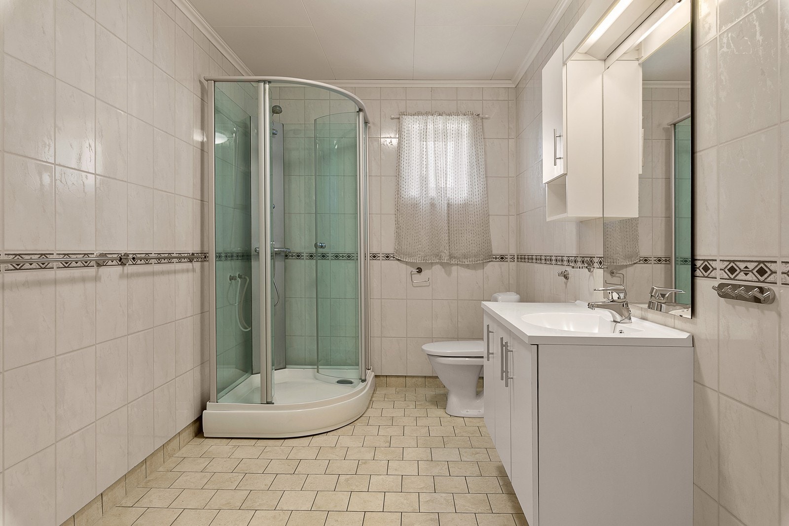 Romslig og funksjonelt bad med flislagte gulv som har varmekabler. Badet er innredet med dusjkabinett, toalett og baderomsinnredning med servant og speilskap som gir gode oppbevaringsmuligheter. Galleribilde