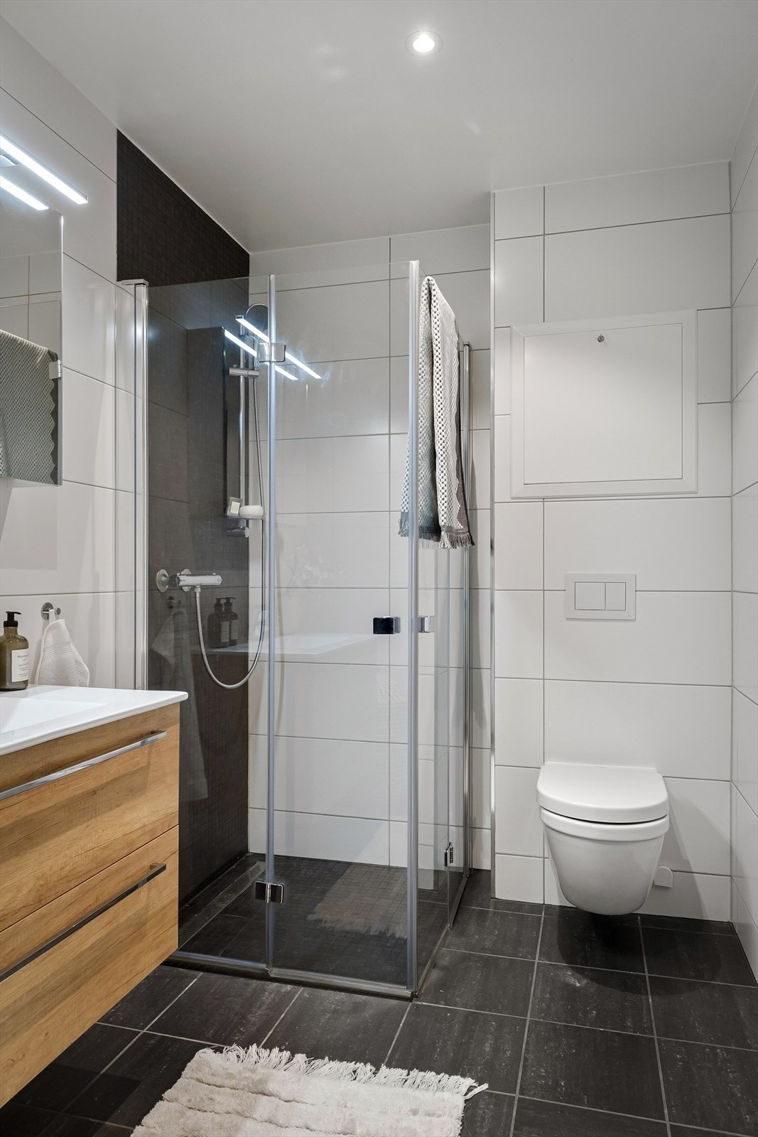 Dusjsonen er markert med mørke mosaikkfliser. Badet har vegghengt toalett og mekanisk avtrekk. Galleribilde
