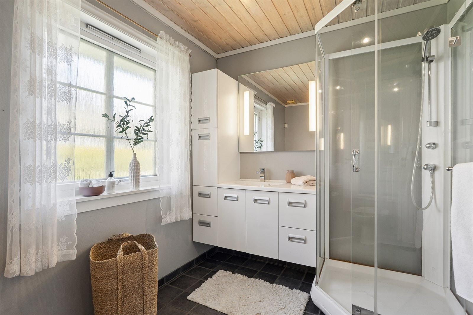 Bad med fliser på gulv, malt strie på vegg og beiset panel i tak. Rommet har baderomsinnredning, dusjkabinett, wc og bidè. Rommet er ventilert med mekanisk ventilasjon i tak og lufteventil i vindu. TG3 i rapporten. Galleribilde