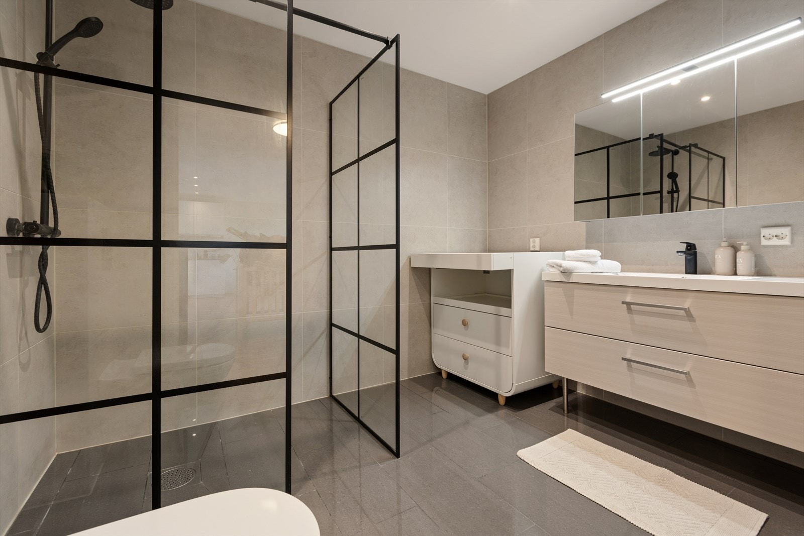 Badet i hovedetasjen er rålekkert med store 60X60 fliser på vegg, m/stor dusj-sone med sorte detaljer og baderomsinnredning med mye skuffeplass, stort speil m/ledd lys. Galleribilde