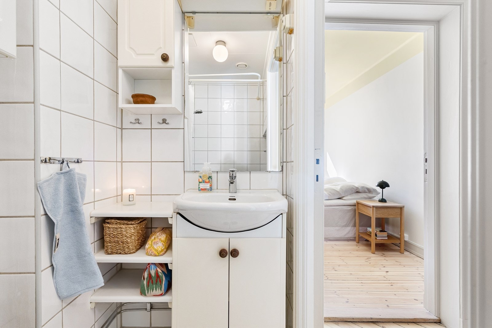 Rommet er utstyrt med gulvstående toalett, dusjhjørne med forheng og baderomsmøbel med skap, hyller, servant og speil. Galleribilde