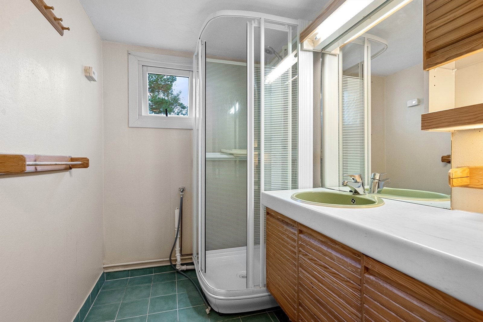 Badet i boligen er innredet med fliser på gulvet, dusjkabinett, servant i skapinnredning, speil med belysning og opplegg for vaskemaskin. Galleribilde