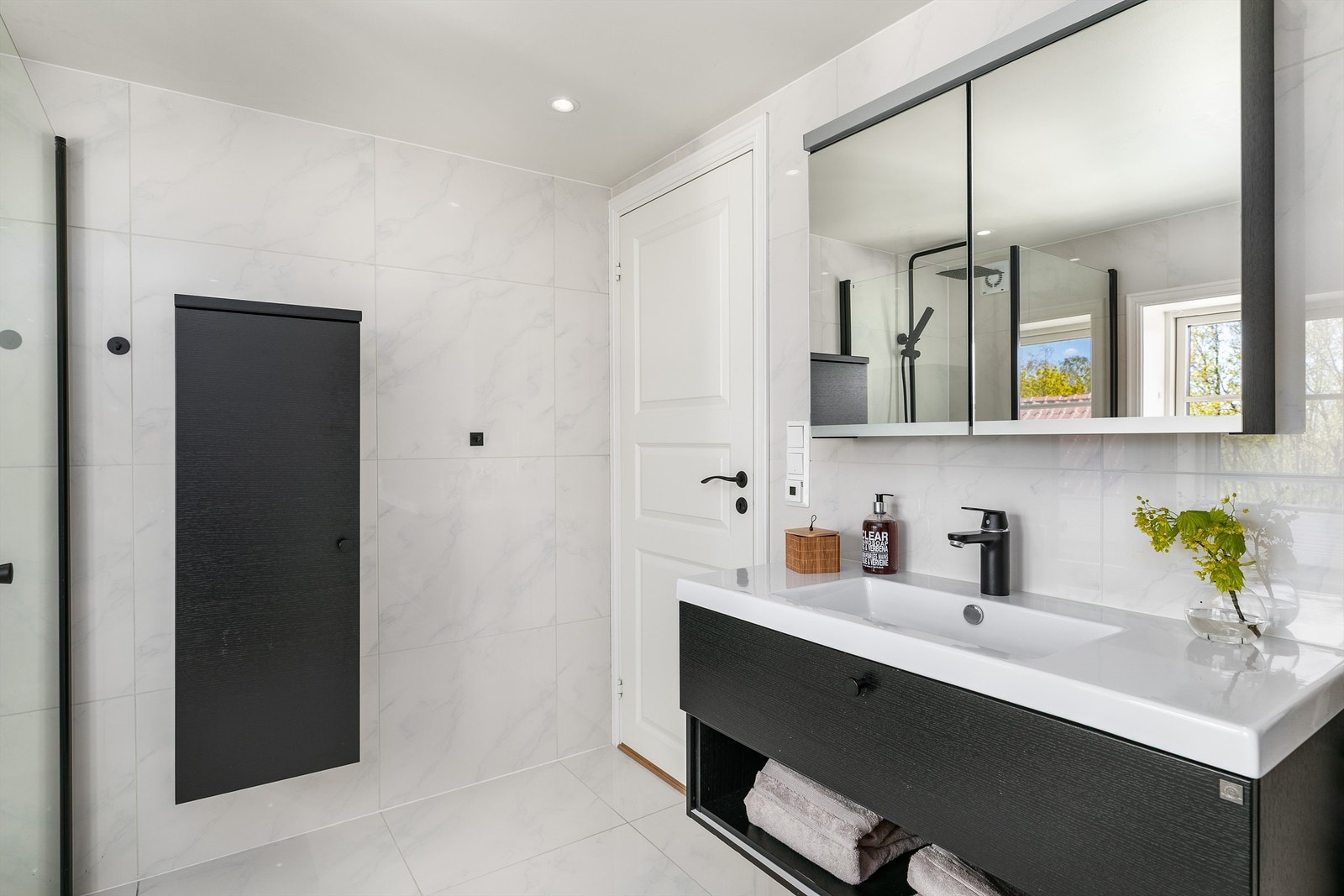 I loftsetasjen inngår også hovedbadet, med marmorerte hvite storformat fliser på gulv og vegger mot møbler og garnityr i kontrasterende sort. Galleribilde