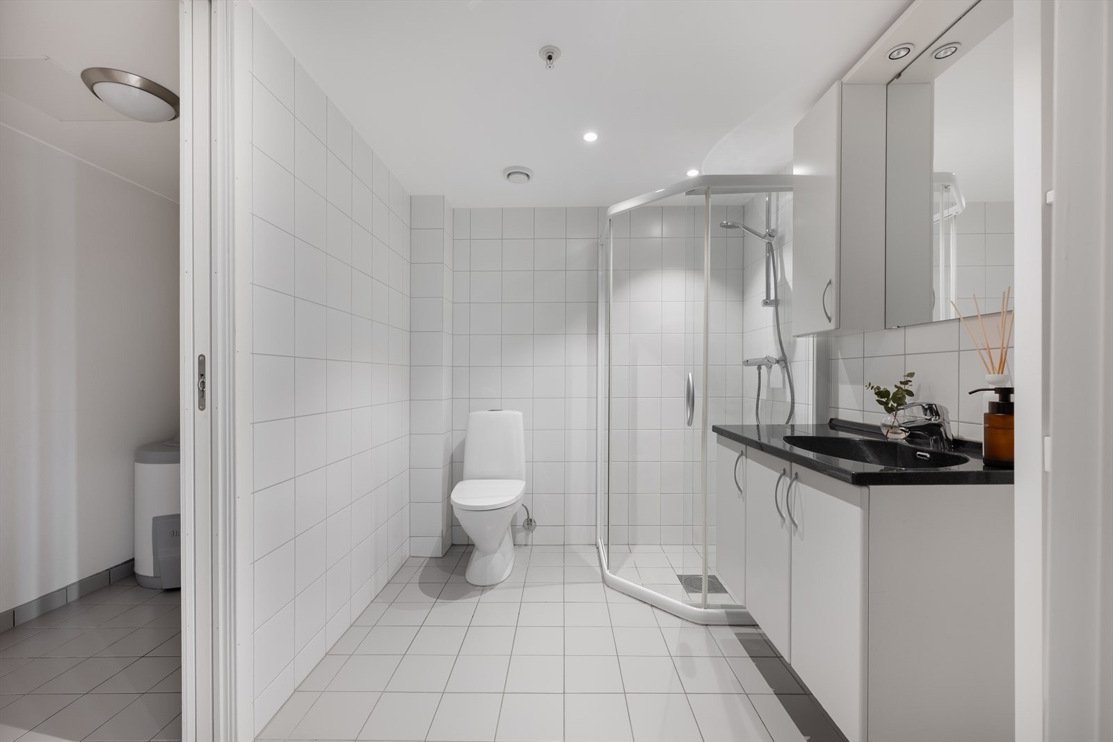 Badet er tidløst innredet med lyse fliser på gulv og vegger. I gulvet har man også varmekabler for ekstra komfort. Badet er ellers utstyrt med dusjhjørne, toalett og baderomsinnredning med god lagringsplass og nedfelt servant. Galleribilde