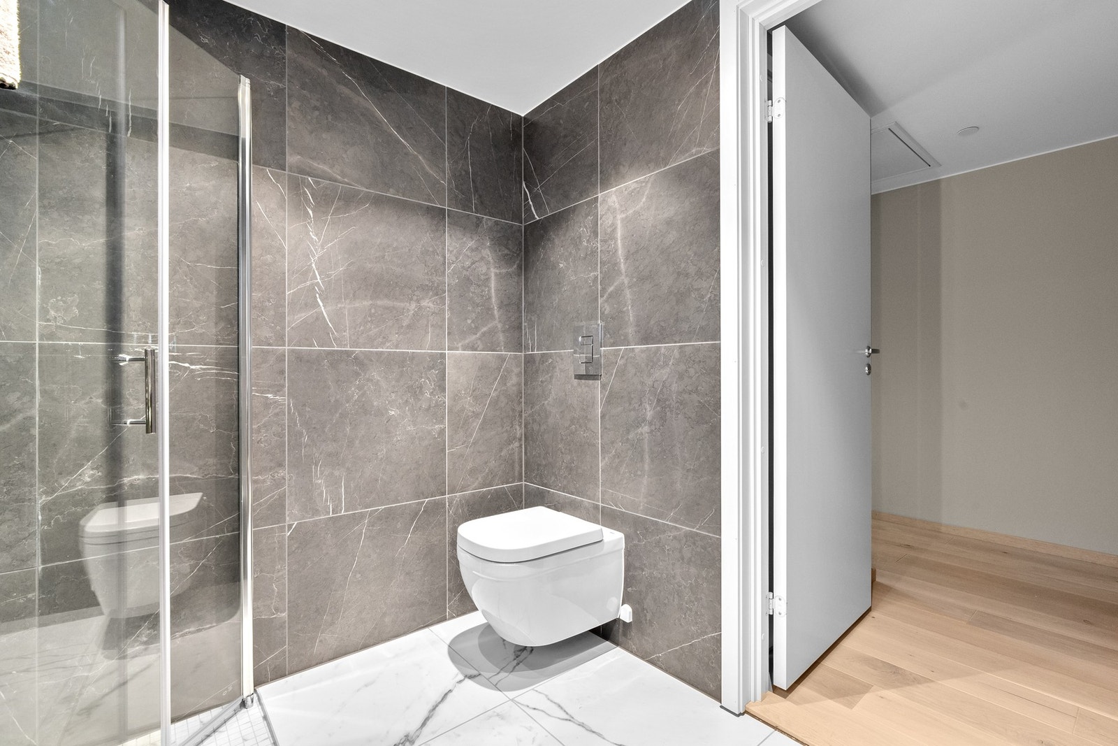 Badet er utstyrt med vegghengt toalett, romslig dusjsone med glassvegger og moderne armaturer. Galleribilde