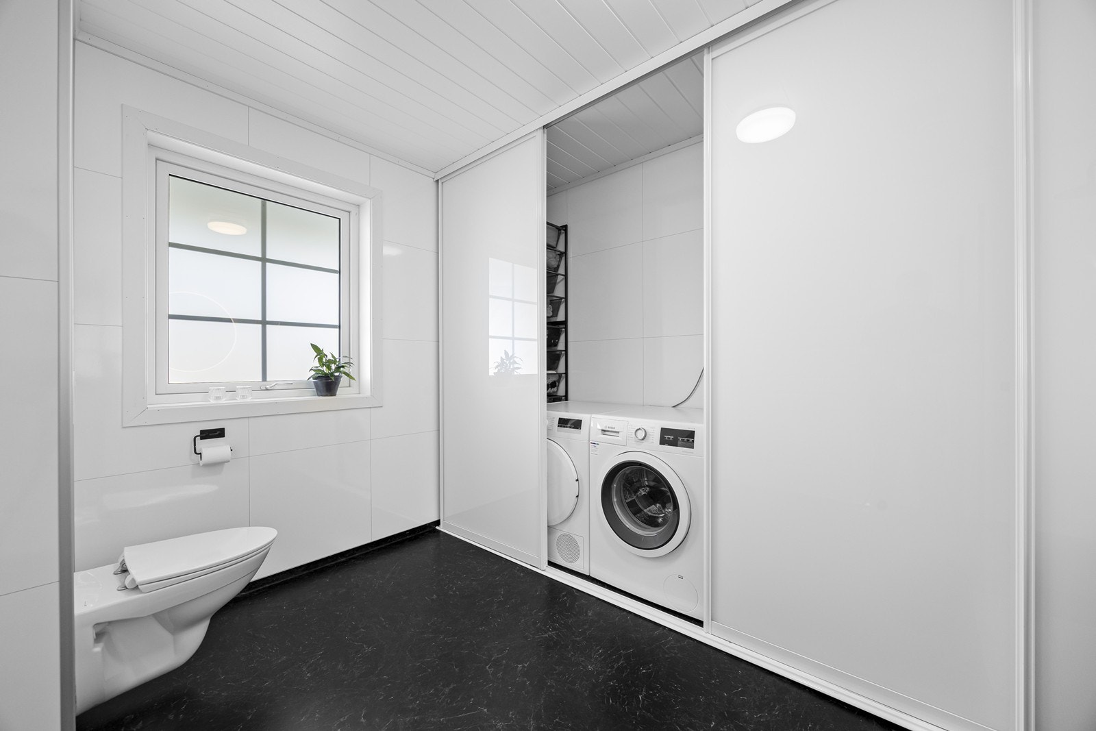 Bad/vaskerom har plass til vaskemaskin og tørketrommel bak skyvedører. Her er det også god plass til oppbevaring. Galleribilde