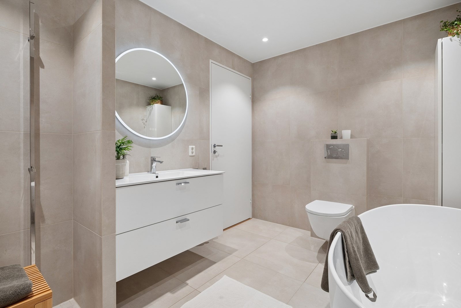 Badet er utstyrt med vegghengt toalett, dusj med glassvegg, badekar, veggskap, samt baderomsinnredning med servant og speil. Galleribilde