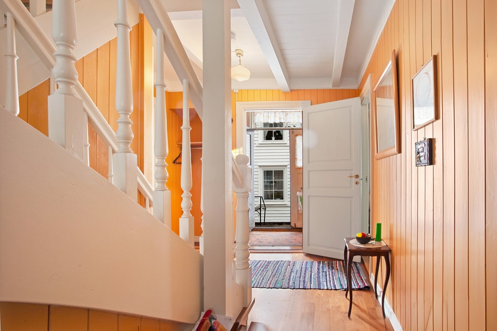 Velkommen inn. Hallen har parkett på gulvet og en innvendig trapp i tre som forbinder etasjene. Galleribilde
